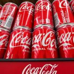 Many Coca-Cola cans stacked on top of each other on a supermarket display stand