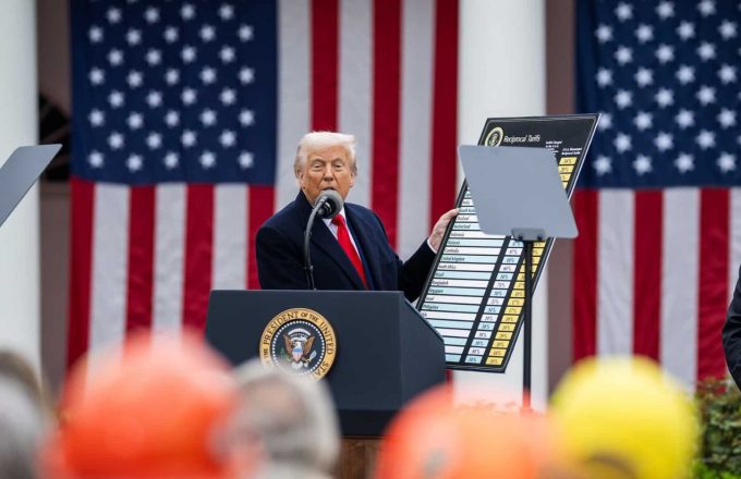 Trump standing on stage showing his audience the big tariff chart for different countries