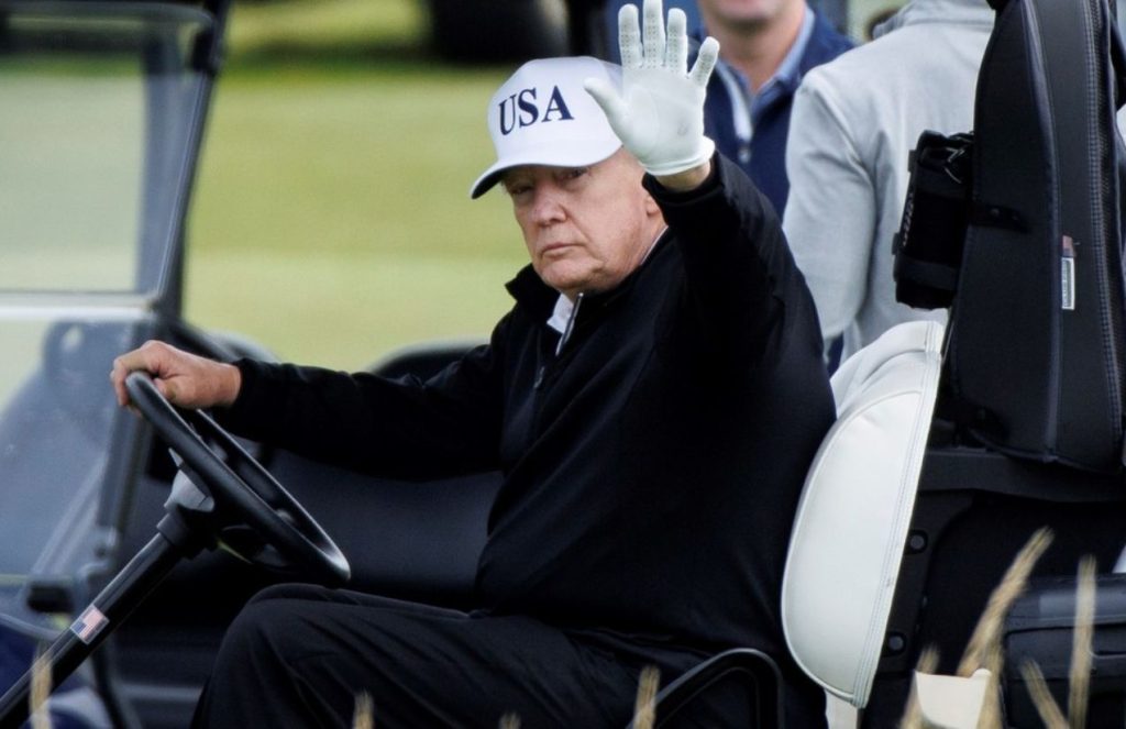Trump waving to the public while driving a golf cart during his visit to Scotland
