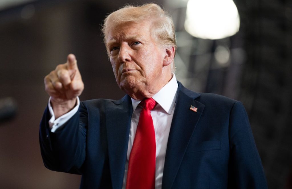 Donald Trump wearing an elegant suit, pointing forward with a very serious expression on his face