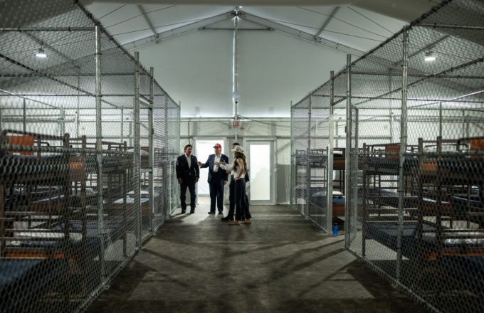 Several people standing in the middle of an alleyway lined with cells on both sides where undocumented immigrants are being held