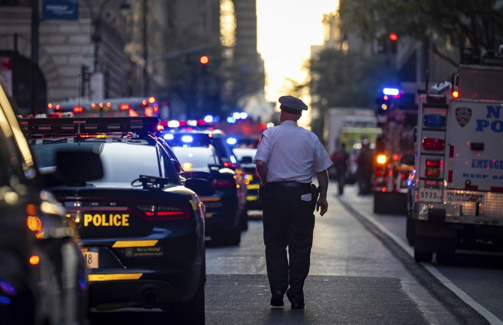 A police officer walking down the middle of a street lined with cars on both sides