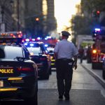 A police officer walking down the middle of a street lined with cars on both sides