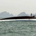 A capsized boat with some people trying to climb onto the hull to avoid drowning