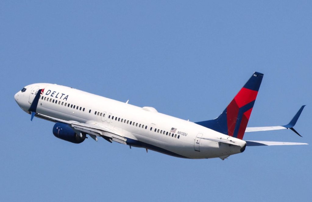 A white Delta Airlines plane flying across a vast blue sky