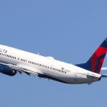 A white Delta Airlines plane flying across a vast blue sky