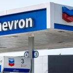 A gas station with the word "Chevron" in white letters against a sky-blue background