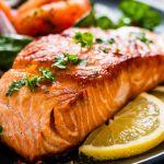 A delicious piece of cooked salmon served on a plate, accompanied by lemons and vegetables on the side