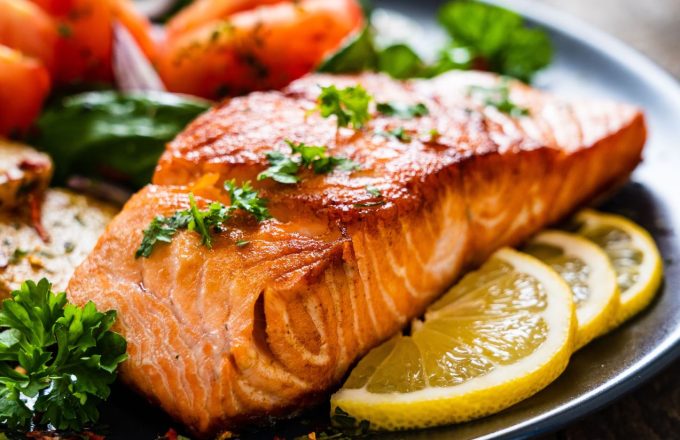 A delicious piece of cooked salmon served on a plate, accompanied by lemons and vegetables on the side