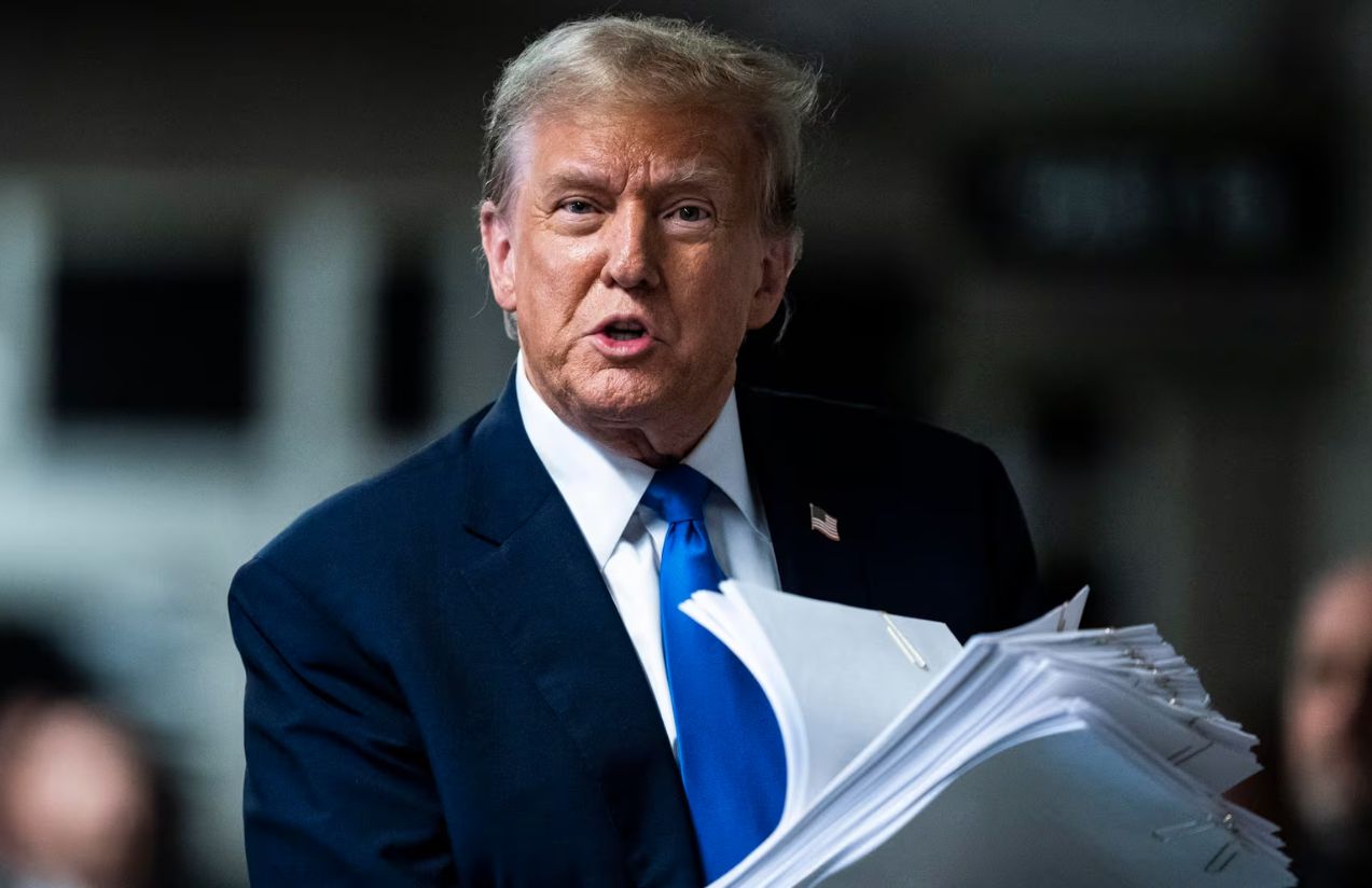 Donald Trump holding several documents in his left hand with a slightly annoyed expression