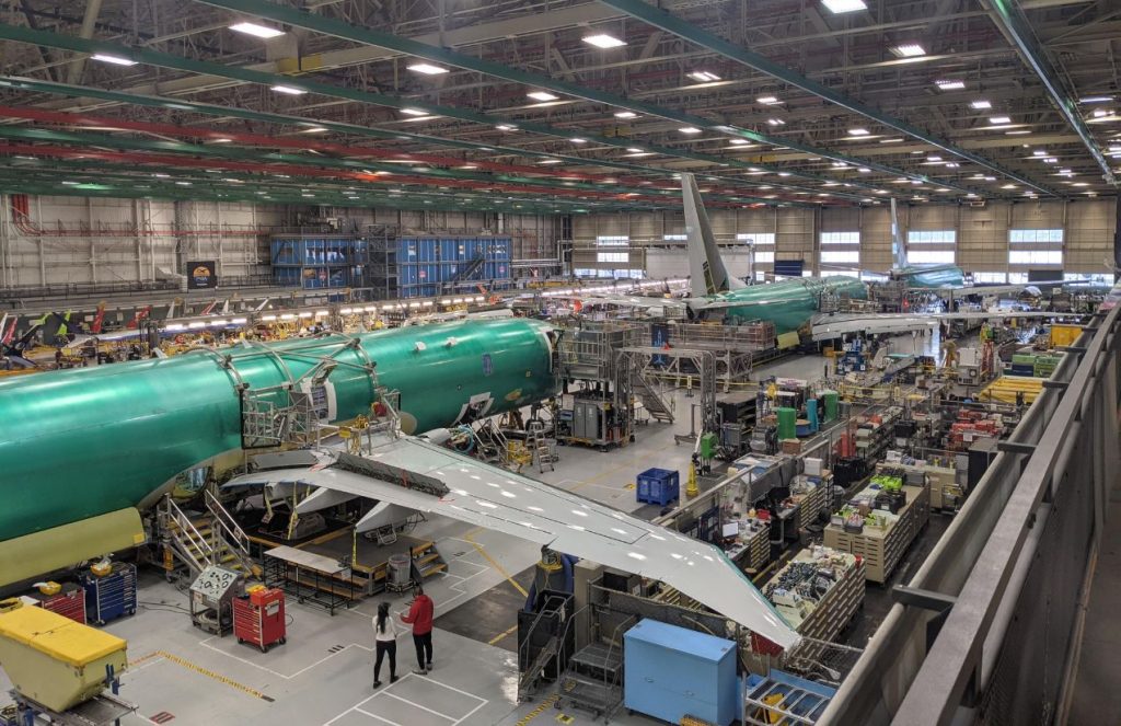 An aircraft assembly plant bustling with many workers actively building and inspecting airplanes