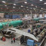 An aircraft assembly plant bustling with many workers actively building and inspecting airplanes