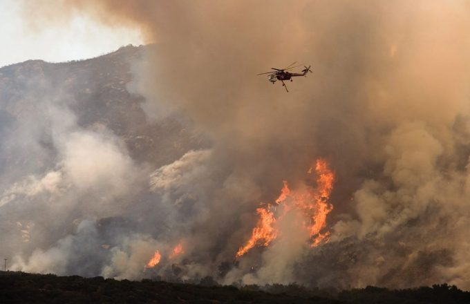 A helicopter hovering over a massive forest fire, trying to drop water on the flames