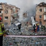 A half-destroyed building surrounded by several firefighters trying to help with the tragedy