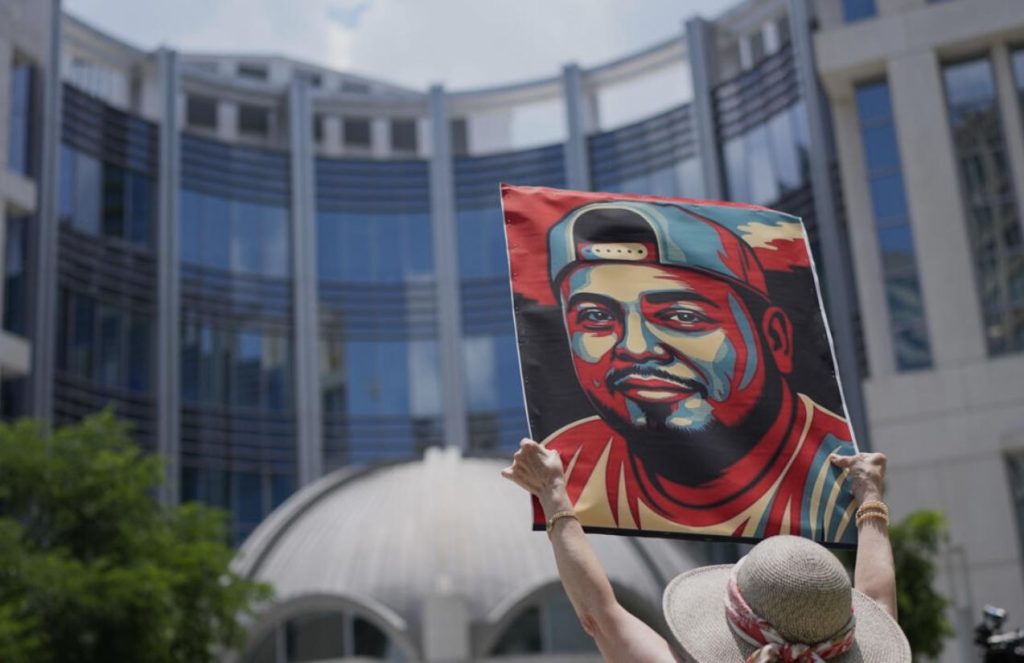 Kilmar Ábrego García, released in Tennessee after wrongful deportation: Awaits trial under house arrest A young woman raising a portrait of Kilmar with both arms in the middle of a crowd of people