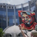 A young woman raising a portrait of Kilmar with both arms in the middle of a crowd of people