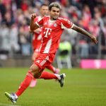 Luis Díaz running across the field in Bayern’s striking new red uniform while looking happy