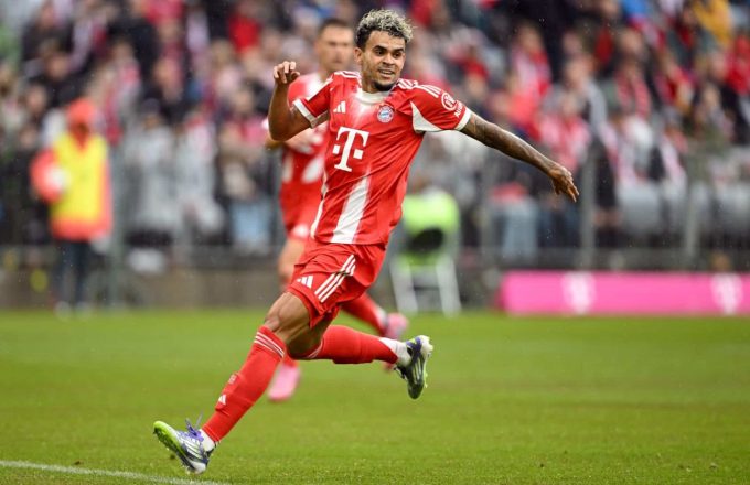 Luis Díaz running across the field in Bayern’s striking new red uniform while looking happy