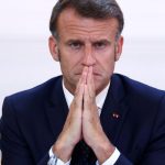 Emmanuel Macron sitting at his desk with his hands clasped in front of his nose