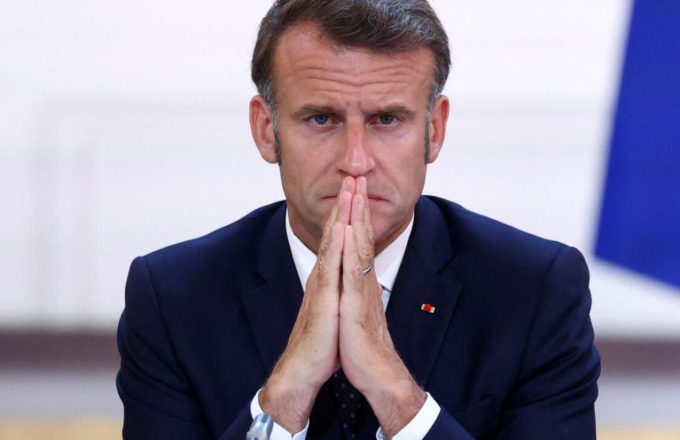 Emmanuel Macron sitting at his desk with his hands clasped in front of his nose