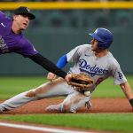 A Rockies player stretching his arm across the ground to catch the ball and tag the Dodgers player