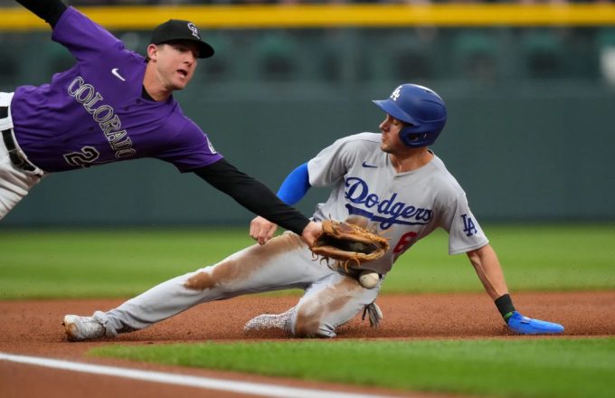 A Rockies player stretching his arm across the ground to catch the ball and tag the Dodgers player