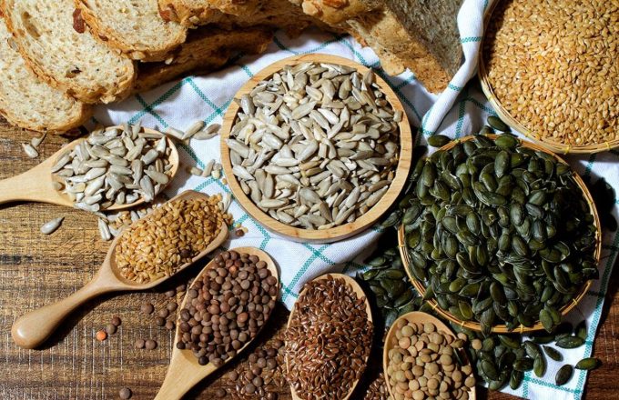 Different types of seeds piled up in spoons of various sizes=