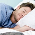 A man lying in bed with his eyes closed and smiling