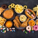 A table with various examples of ultra-processed foods such as burgers, French fries, sausages, and desserts