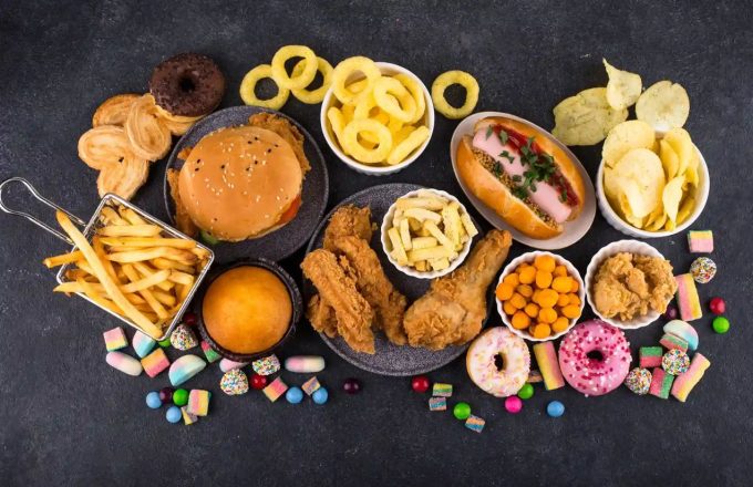 A table with various examples of ultra-processed foods such as burgers, French fries, sausages, and desserts