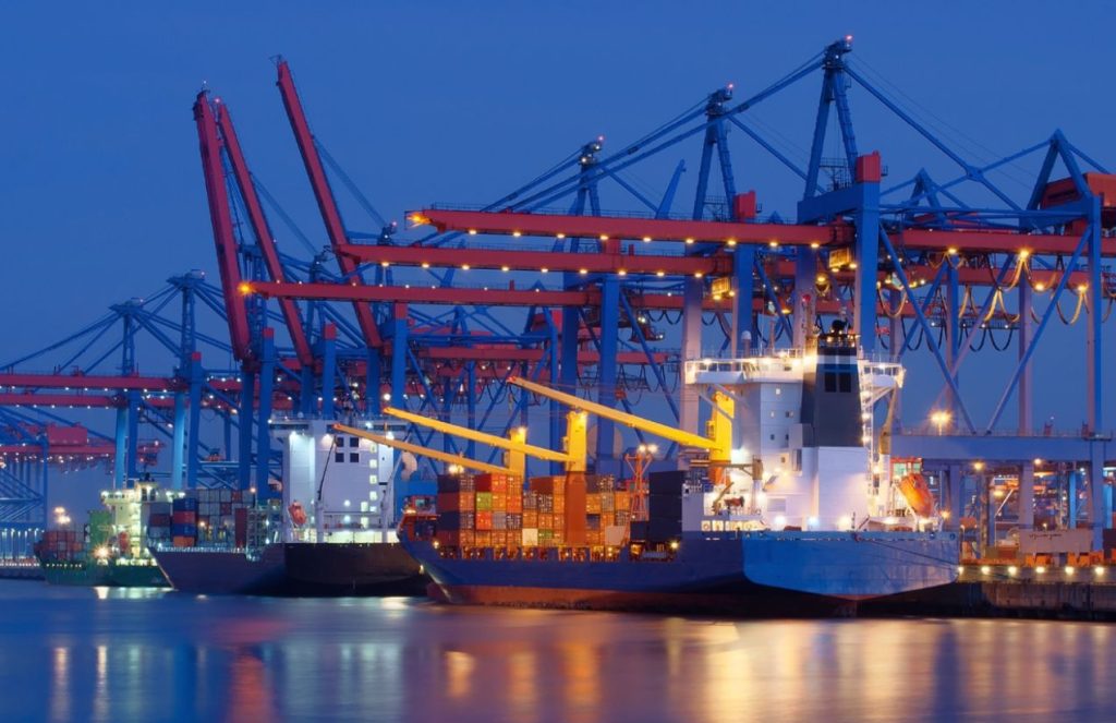 A massive ship docked at a port, being loaded with containers to transport them to their destination