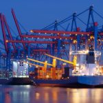 A massive ship docked at a port, being loaded with containers to transport them to their destination