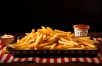 A plate of French fries served on a black dish, accompanied by two sauces on the side