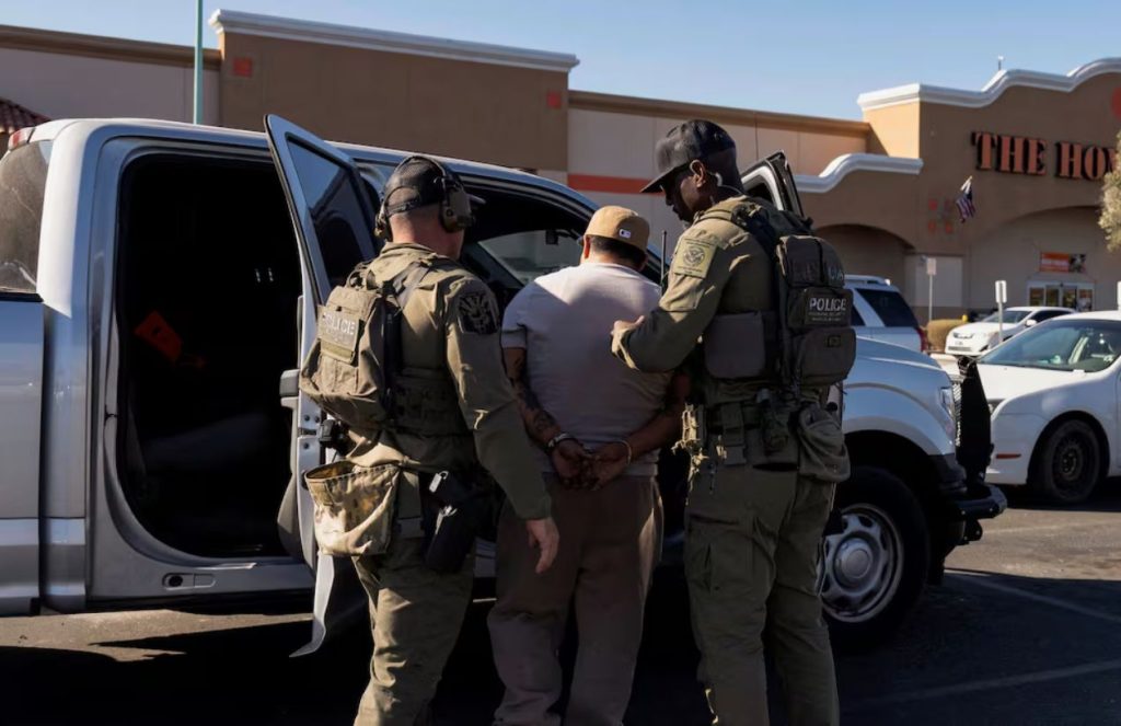 Two federal police officers handcuffing an alleged immigrant while placing him in their car