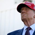 Donald Trump wearing a formal suit complemented by a red cap with the words "Make America Great Again."
