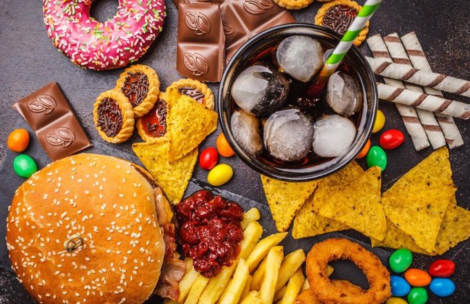 A table with various ultra-processed foods such as sweets, Coca-Cola, and hamburgers