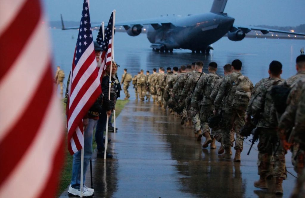 A row of U.S. soldiers heading toward a military plane with their uniforms and weapons