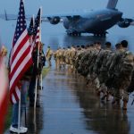 A row of U.S. soldiers heading toward a military plane with their uniforms and weapons
