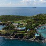 An image of the luxurious island showing a white mansion with blue roofs and an ocean view