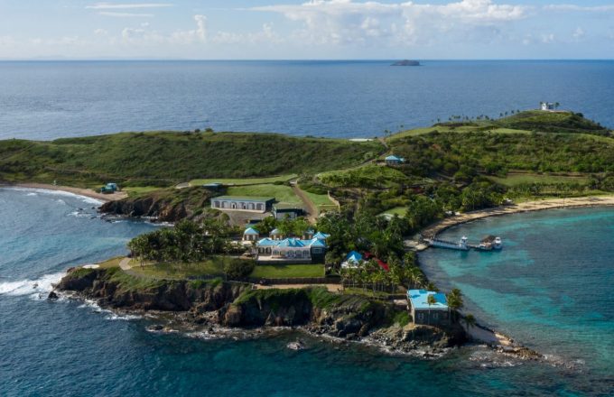 An image of the luxurious island showing a white mansion with blue roofs and an ocean view
