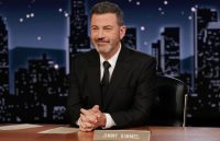 Kimmel sitting at his show’s desk wearing an elegant black suit