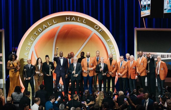 NBA players posing on the Hall of Fame stage holding their trophies and golden jackets