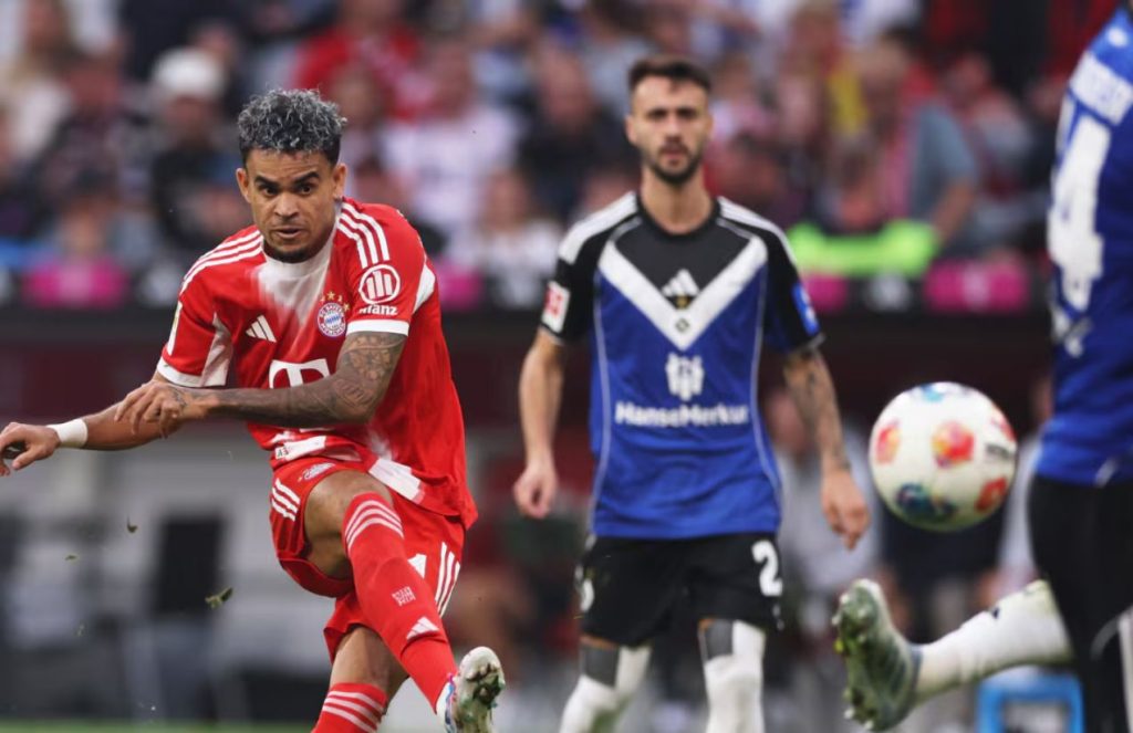 The Colombian player kicking the ball toward the goal while wearing his purple boots and his team’s full uniform