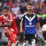 The Colombian player kicking the ball toward the goal while wearing his purple boots and his team’s full uniform