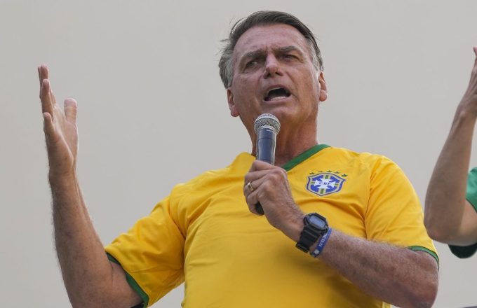 Bolsonaro wearing the Brazil jersey and holding a microphone while speaking to the crowd