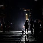 Several kids walking in the darkness of the streets of Cuba, their silhouettes clearly visible thanks to the reflection of a distant lamp