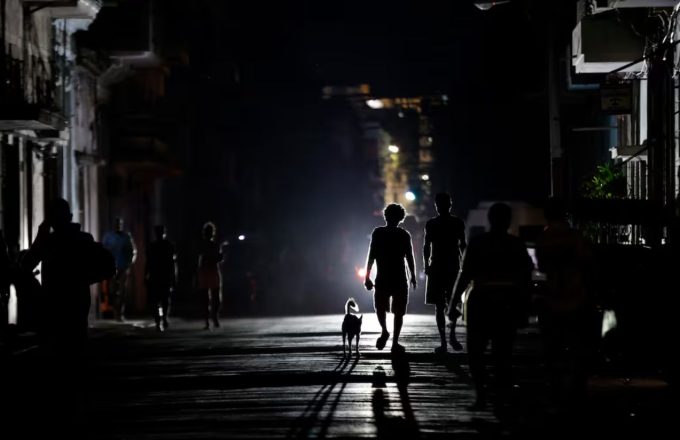 Several kids walking in the darkness of the streets of Cuba, their silhouettes clearly visible thanks to the reflection of a distant lamp