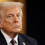 Trump casting a threatening yet confident look at the crowd while wearing an elegant black suit