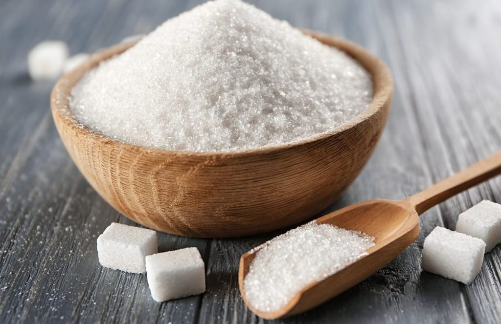 A bowl of sugar on a table next to several small sugar cubes