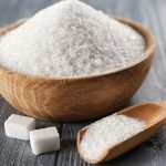 A bowl of sugar on a table next to several small sugar cubes